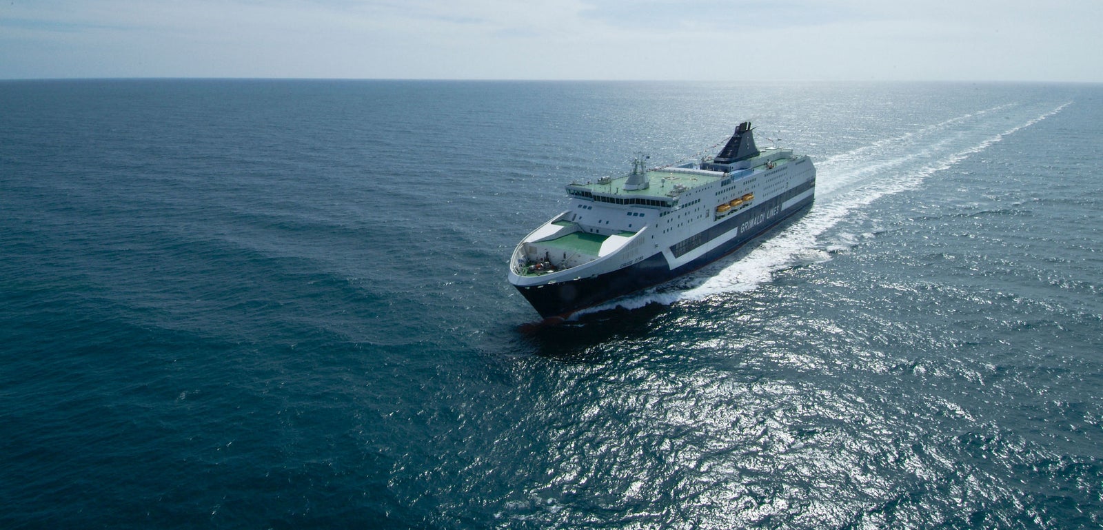 Fincantieri | Group - Business - Products - Ferries - Cruise Roma: Large ferry with "Brittany Ferries" text in operation, sleek design, multiple decks, cruising through open ocean, partly cloudy sky in background.