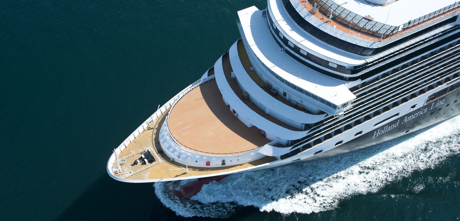 Fincantieri | Group - Business - Products - Cruise Ships - Nieuw Amsterdam: Aerial view of large Holland America Line cruise ship in operation sailing on deep blue ocean waters, multiple decks including open sun deck at bow, visible white wake highlighting dynamism and scale.