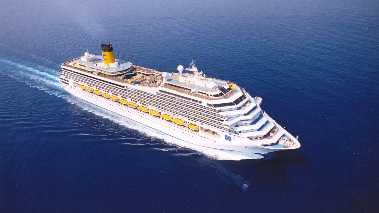 Fincantieri | Gruppo - Business - Prodotti - Navi da Crociera - Costa Magica: Vista laterale della nave Costa Magica operativa in navigazione, scafo con ponti passeggeri multipli, scialuppe gialle visibili e aree esterne sui ponti superiori.