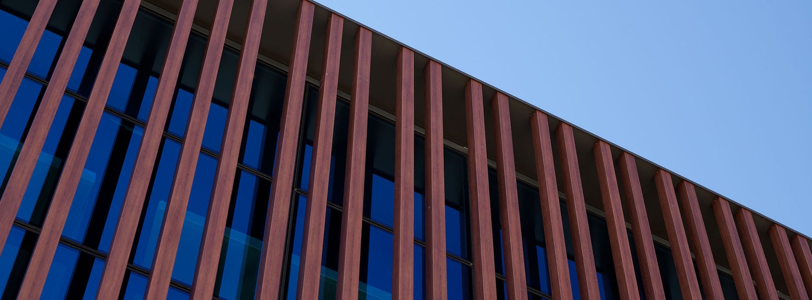 Fincantieri | Products - Ship Interiors - Contemporary Architecture: Modern building with reddish-brown vertical panels and large reflective glass windows, elegant design and clean lines in a bright outdoor setting under a blue sky.
