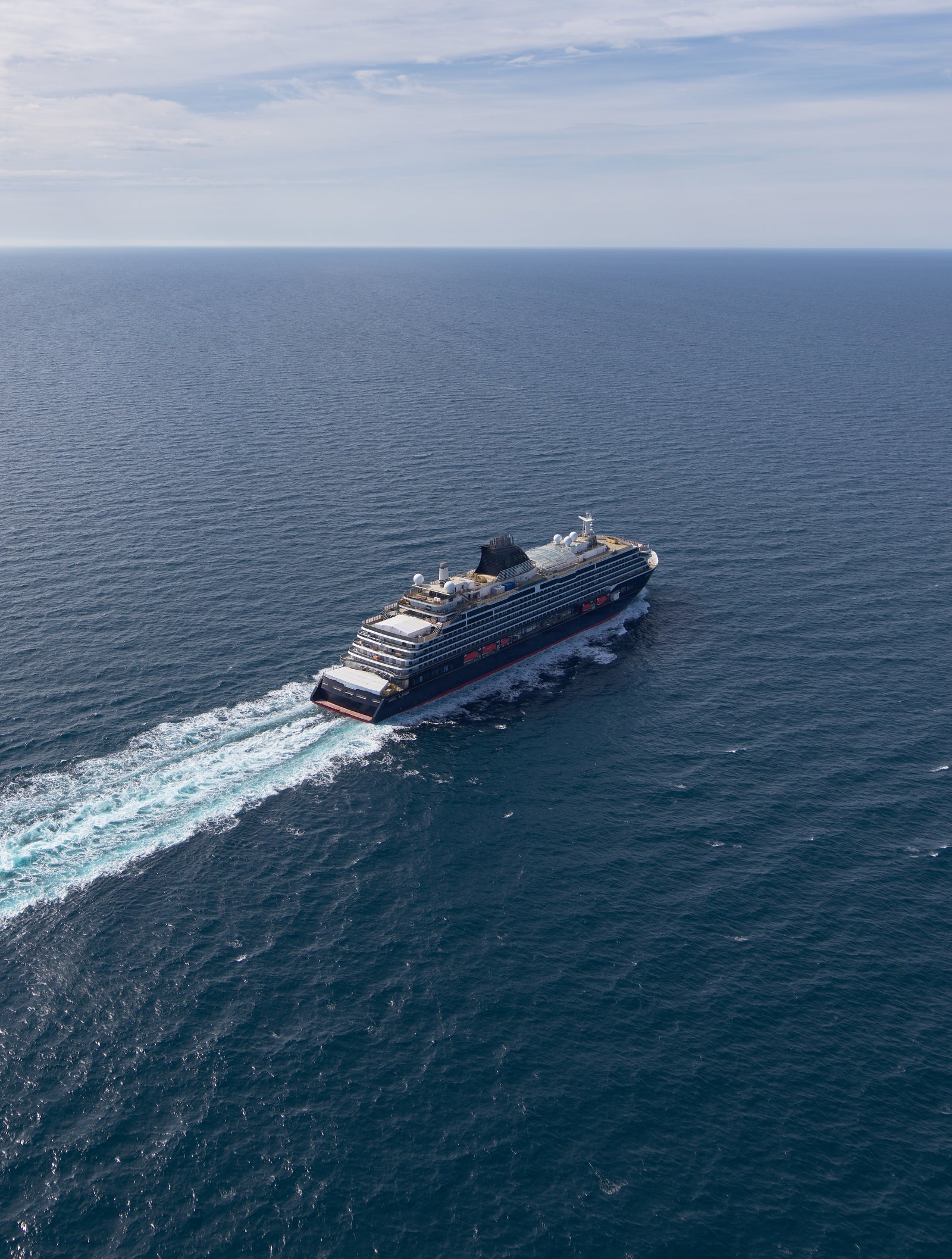 Fincantieri | Group - Business - Products - Cruise Ships - Explora I: Large cruise ship in operation, traveling across calm open ocean, bright blue sky with scattered clouds, visible white wake, serene setting emphasizing sea vastness.