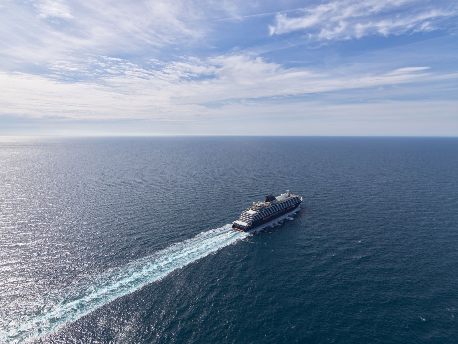 Fincantieri | Group - Business - Products - Cruise Ships - Explora I: Large cruise ship in operation, traveling across calm open ocean, bright blue sky with scattered clouds, visible white wake, serene setting emphasizing sea vastness.