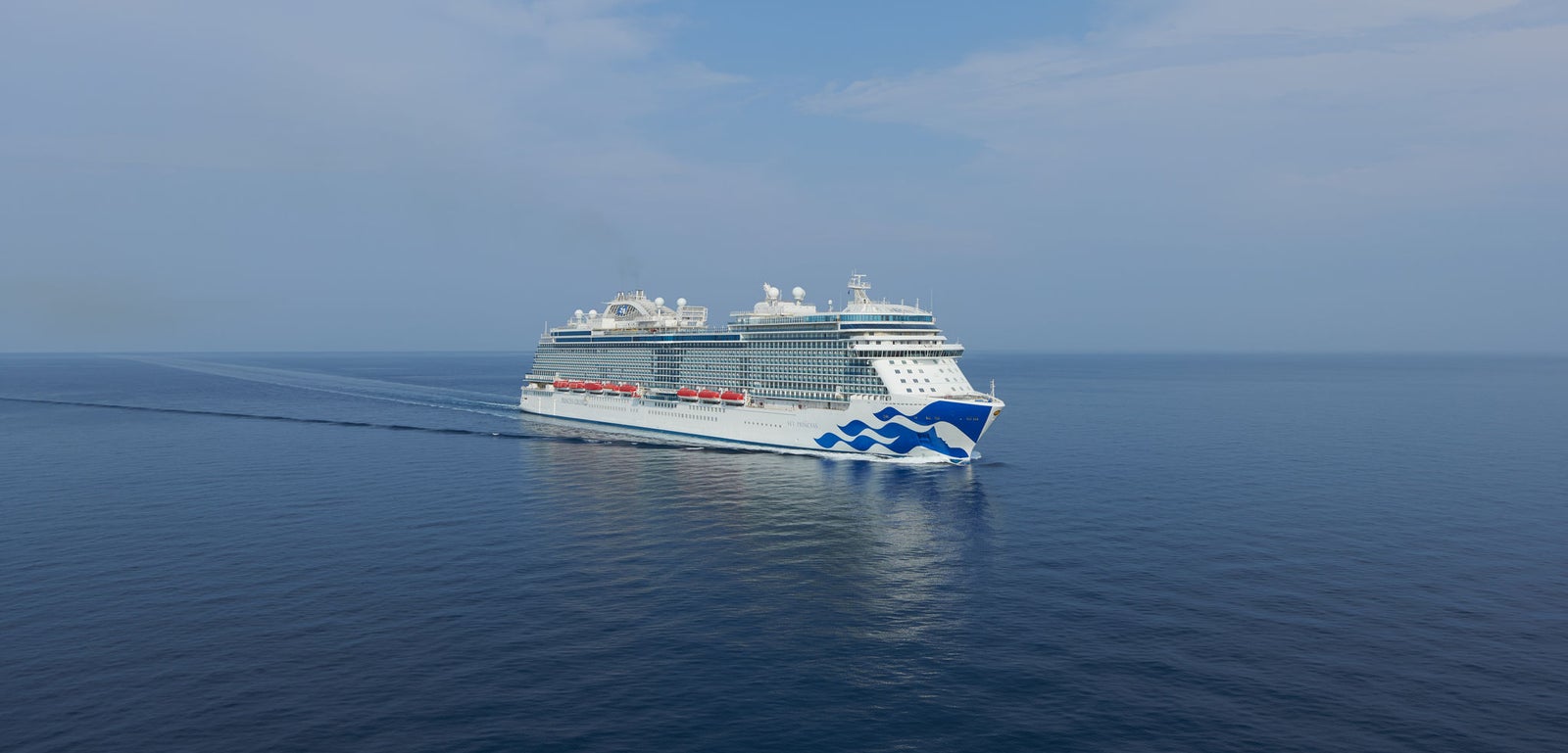 Fincantieri | Gruppo - Business - Prodotti - Navi da Crociera - Sky Princess: Grande nave da crociera di lusso operativa che naviga su acque calme e aperte sotto cielo parzialmente nuvoloso, design a onda sullo scafo e più ponti con servizi visibili.