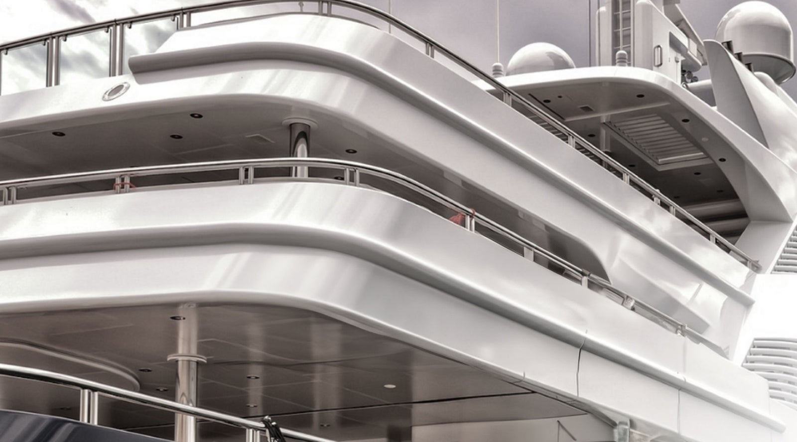 Fincantieri | Group - Subsidiaries and Affiliates - SLS: Close-up view of a sleek luxury yacht with modern architectural design, polished metallic surfaces and curved railings; sophisticated scene, overcast skies in the background.