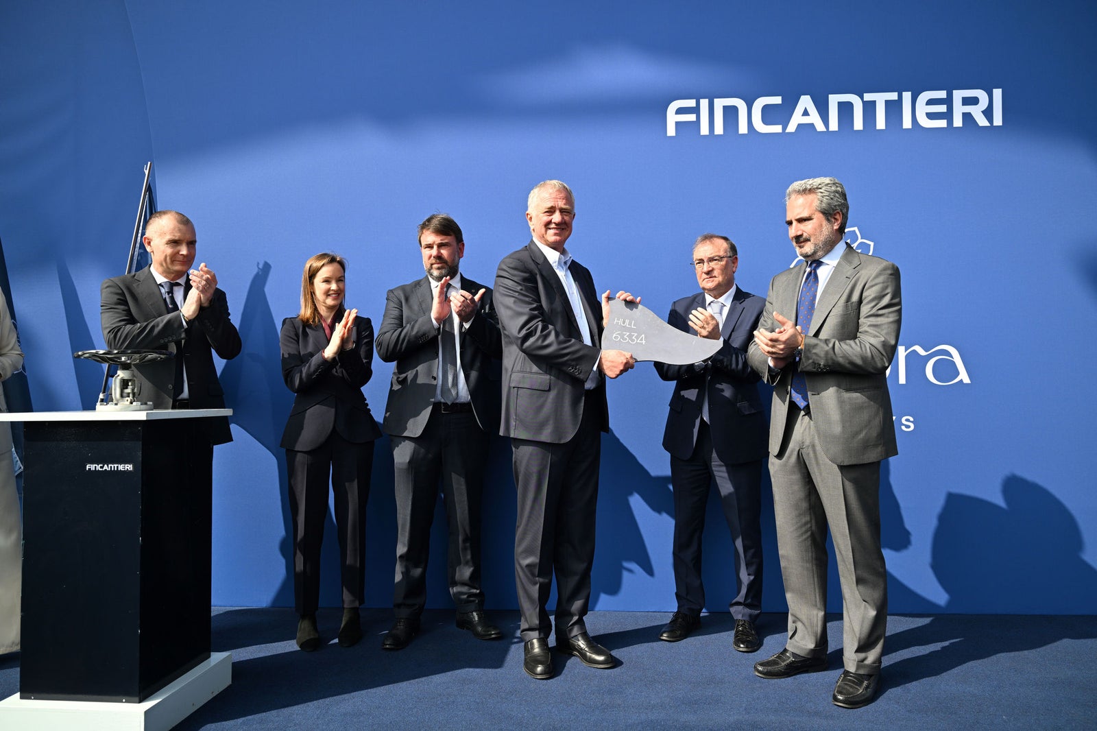 Newsroom - Press releases - 2026 - Fincantieri Group: Fincantieri:  Today triple ceremony for Fincantieri and Explora Journeys at Sestri Ponente: launche of Explora IV, coin ceremony for Explora V and steel cuttingfor Explora VI: Fincantieri and Explora managers in suits celebrate coin ceremony on stage with commemorative hull plate.