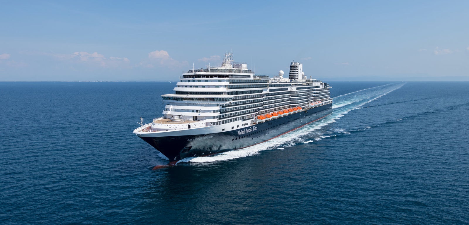  Fincantieri | Gruppo - Business - Prodotti - Navi da Crociera - Nieuw Statendam: Grande nave da crociera, operativa in navigazione su acque calme e aperte sotto cielo azzurro limpido, più ponti e scialuppe di salvataggio visibili lungo i lati.