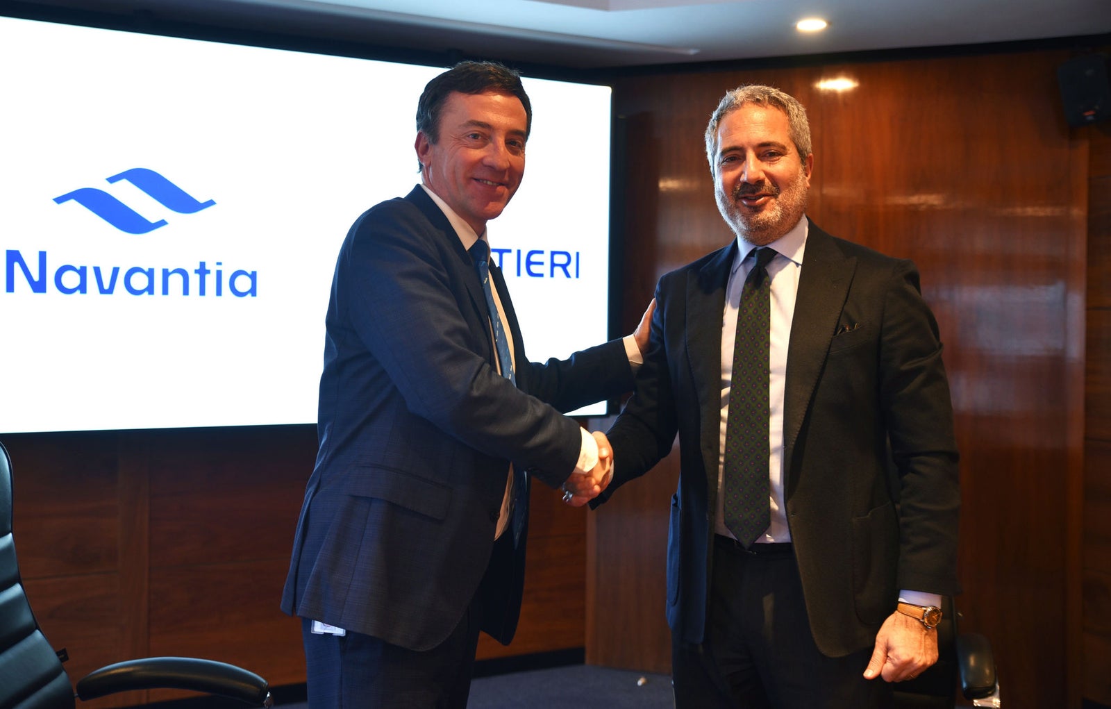 Newsroom - Press releases - 2026 - Fincantieri Group: Navantia and Fincantieri strengthen their cooperation to advance the European Patrol Corvette (EPC) programme: navantia and fincantieri executives in suits shake hands in front of presentation screen during epc partnership event.