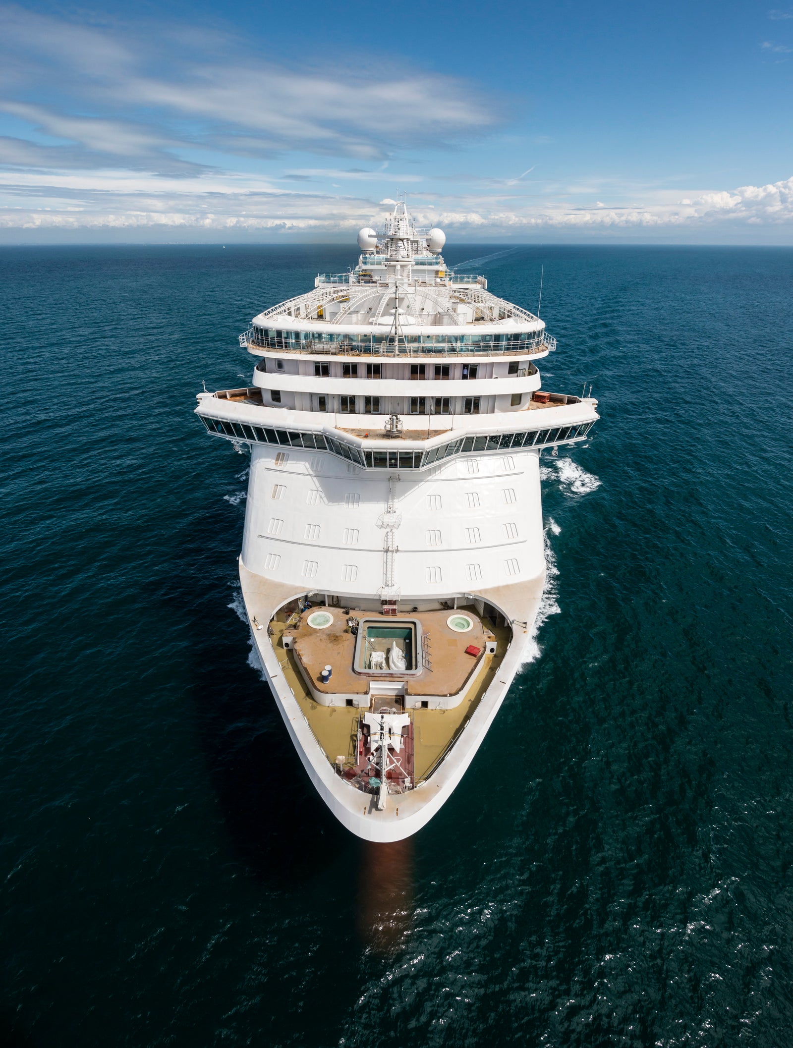 Fincantieri | Group - Business - Products - Cruise Ships - Royal Princess: Aerial front view of large white luxury cruise ship in operation sailing on deep calm blue waters, multiple decks with outdoor relaxation spaces and recreation areas.
