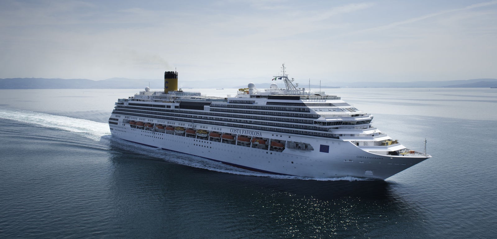  Fincantieri | Group - Business - Products - Cruise Ships - Costa Favolosa: Massive white cruise ship gliding through calm open waters under clear blue sky, multiple decks and distinctive yellow funnel with black top, serene setting highlights ship’s grandeur and ocean vastness.