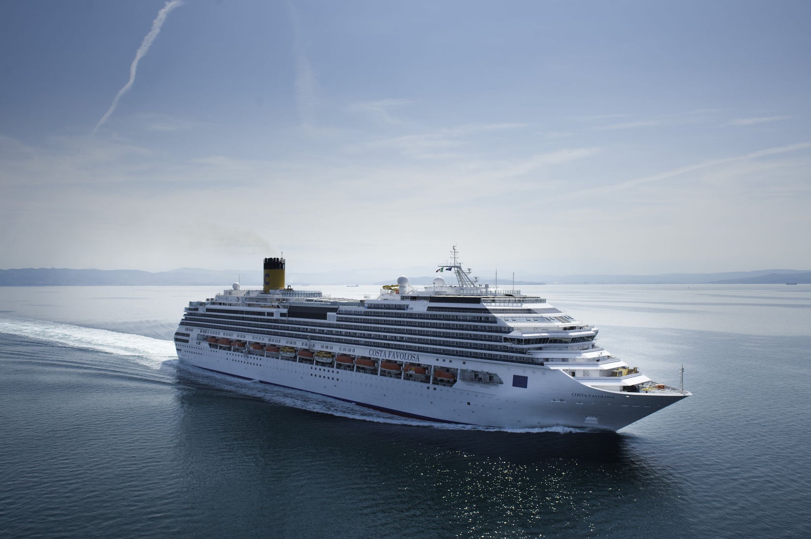 Fincantieri | Group - Business - Products - Cruise Ships - Costa Favolosa: Massive white cruise ship gliding through calm open waters under clear blue sky, multiple decks and distinctive yellow funnel with black top, serene setting highlights ship’s grandeur and ocean vastness.