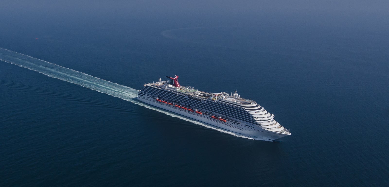 Fincantieri | Group - Business - Products - Cruise Ships - Carnival Breeze: Large operational white cruise ship navigating calm sea under clear sky, multiple decks, distinctive red funnel with Carnival logo, visible wake, scene highlights sea expanse and ship grandeur in a serene environment.