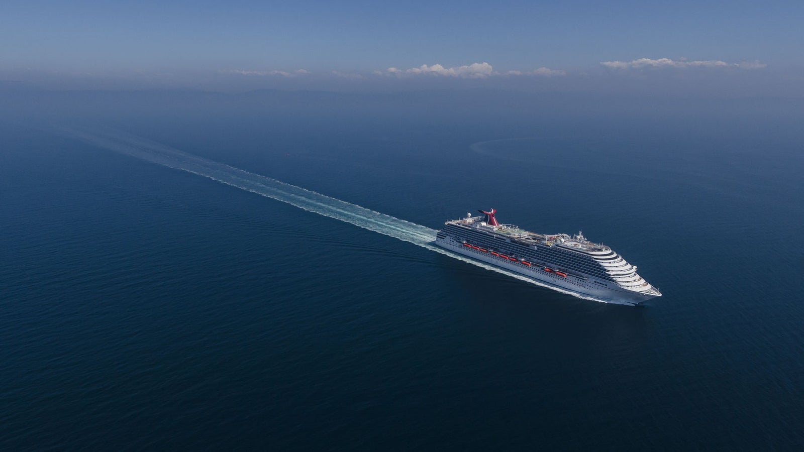 Fincantieri | Group - Business - Products - Cruise Ships - Carnival Breeze: Large operational white cruise ship navigating calm sea under clear sky, multiple decks, distinctive red funnel with Carnival logo, visible wake, scene highlights sea expanse and ship grandeur in a serene environment.