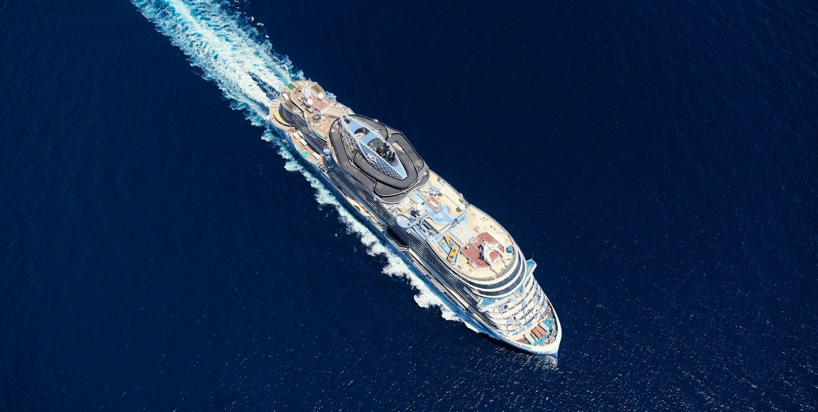 Fincantieri | Group - Business - Products - Cruise Ships - Norwegian Prima: Aerial view of Norwegian Prima cruise ship in operation, multiple decks, pool area, modern design elements, visible white wake.