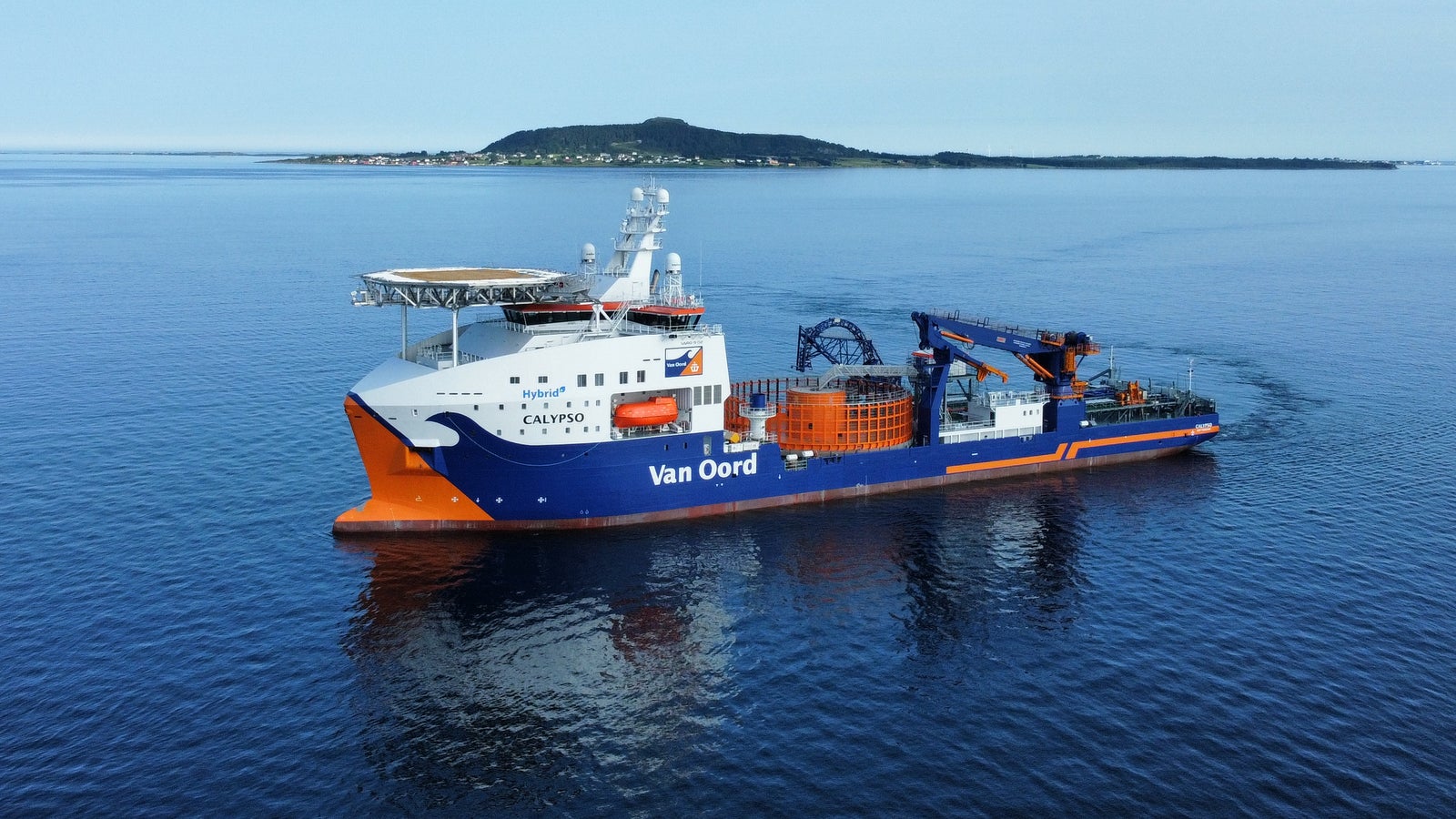 Prodotto - Nave Van Oord Calypso: Vista laterale della nave operativa in navigazione, scafo arancione e blu, equipaggiamenti industriali sul ponte, sfondo con isola distante.
