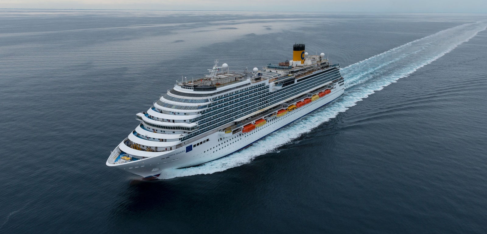 Fincantieri | Group - Business - Products - Cruise Ships - Costa Diadema: View of Costa Diadema cruise ship in operation navigating open sea, visible wake, hull with multiple passenger decks and visible lifeboats.