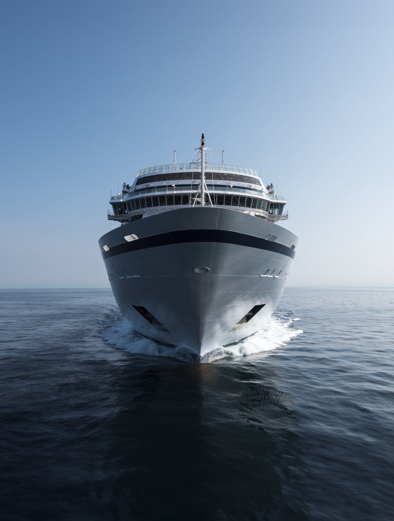 Fincantieri | Group - Business - Products - Cruise Ships - Viking Sky: Front view of Viking Sky cruise ship in operation navigating open sea, linear profile white hull, multiple passenger decks, bow cutting through calm waters under clear sky.