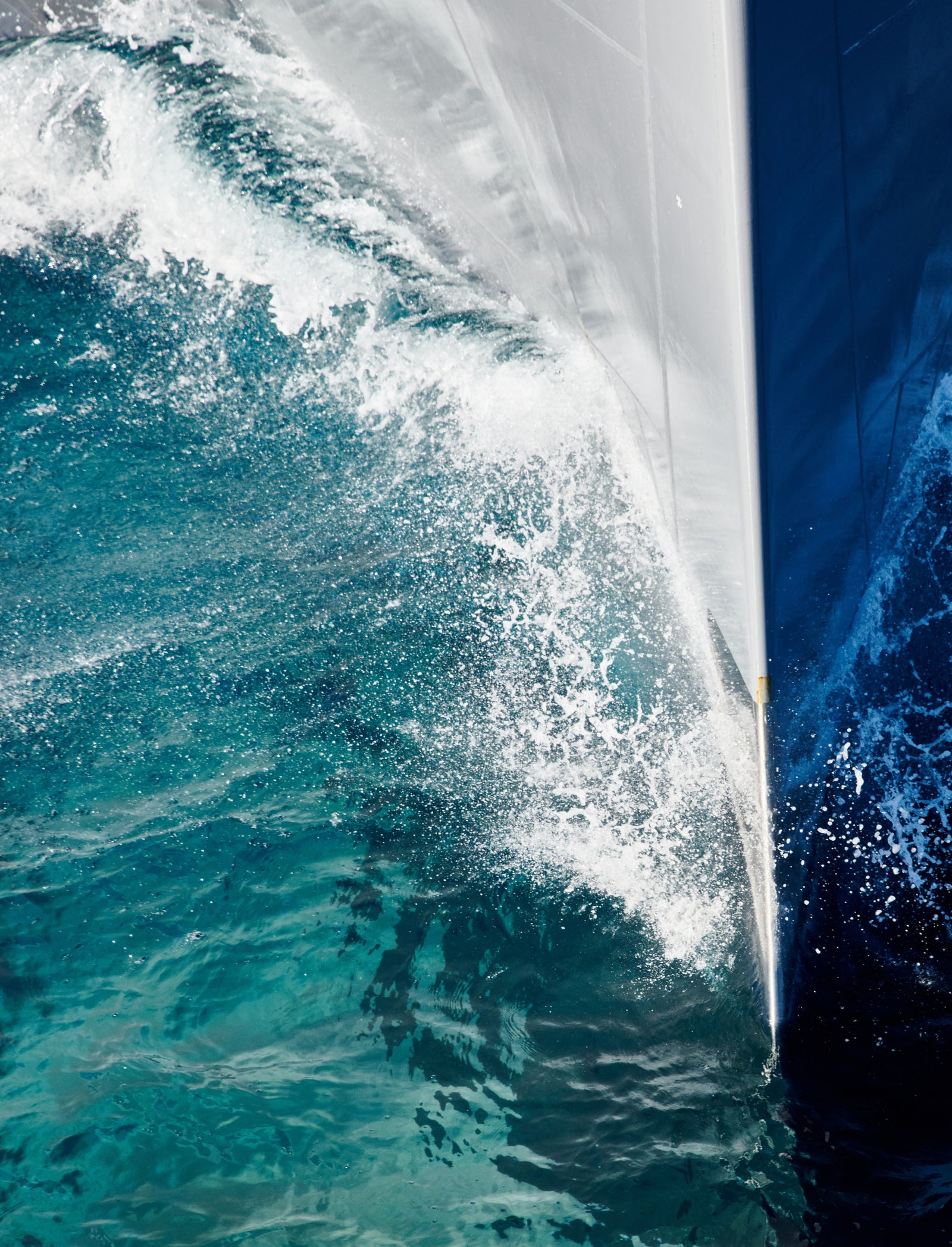Fincantieri | Group - Companies - Subsidiaries and Affiliates - Fincantieri Naval Services: Close-up of the bow of a ship crossing turquoise waters, splashes and ripples around the hull, emphasis on sleek design and dynamic movement in a maritime environment.
