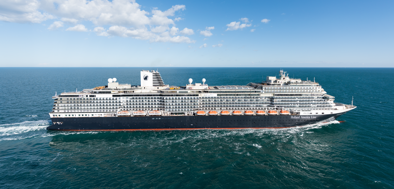Fincantieri | Gruppo - Business - Prodotti - Navi da Crociera - Koningsdam: Grande nave da crociera operativa che naviga su acque calme e aperte sotto cielo azzurro limpido, scia visibile dietro la nave, circondata da ampie viste sull’oceano.