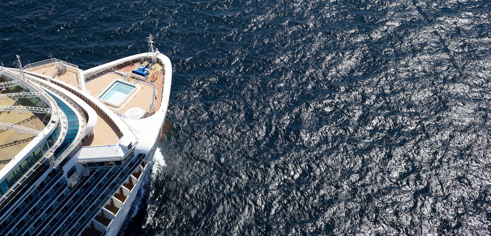 Fincantieri | Group - Business - Products - Cruise Ships - Enchanted Princess: Aerial view of Enchanted Princess cruise ship bow deck in operation, small pool and seating area, ship surrounded by vast sparkling ocean waters under bright sunlight.
