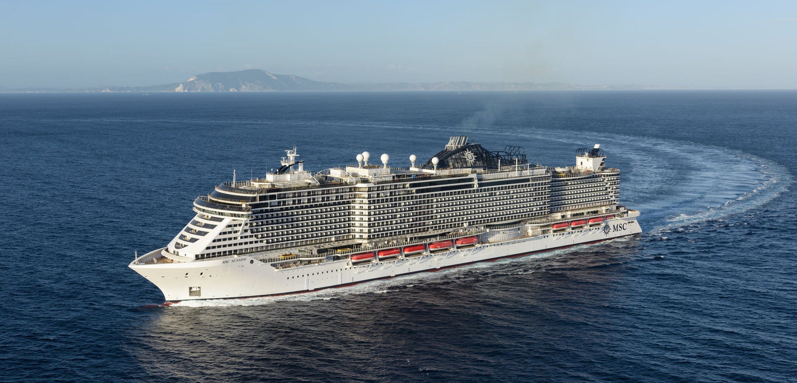 Fincantieri | Group - Business - Products - Cruise Ships - MSC Seaside: Operational cruise ship in navigation with massive hull, multi-level passenger decks, visible lifeboats, coastal profile in background.