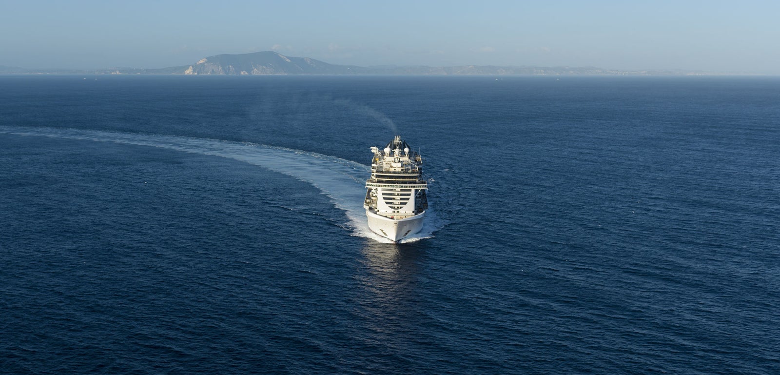 Fincantieri | Group - Business - Products - Cruise Ships - MSC Seaside: Distant view of MSC Seaside cruise ship in operation, multi-level structure and coastal background.