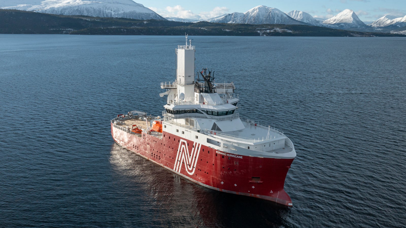 Prodotto - Offshore Support Vessel Norwind Hurricane: Vista laterale della nave operativa in navigazione, scafo rosso con logo N bianco, sovrastruttura bianca, design per operazioni industriali o esplorative, sfondo con montagne innevate.