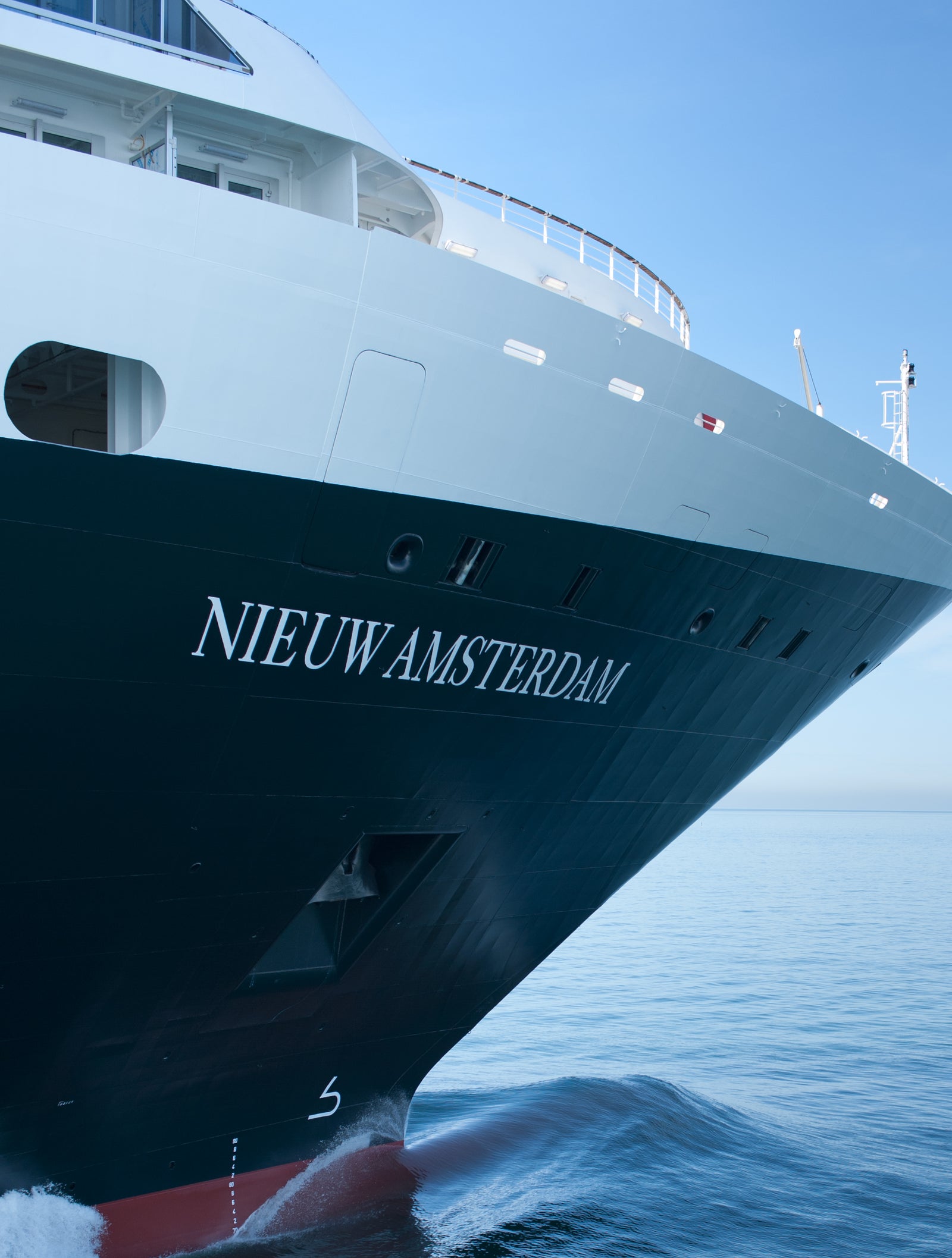 Fincantieri | Group - Business - Products - Cruise Ships - Nieuw Amsterdam: Bow of Nieuw Amsterdam cruise ship in operation clearly visible gliding on serene blue waters, name clearly readable on hull, gentle waves and clear sky create tranquil atmosphere.