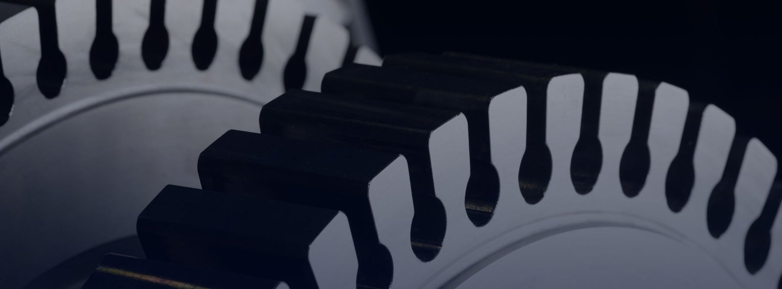 Fincantieri | Group - Sustainability - Energy Transition - Net-zero: Close-up of two interconnected metallic gears, precision engineering with symmetrical teeth and defined edge on a dark background, metallic finish and meticulous workmanship highlighting durability and functionality.Fincantieri | Group - Sustainability - Energy Transition - Net-zero: Close-up detail of two interconnected metallic gears, precision engineering with symmetrical teeth and defined edge on a dark background, metal finish and accurate workmanship highlighting durability and functionality.