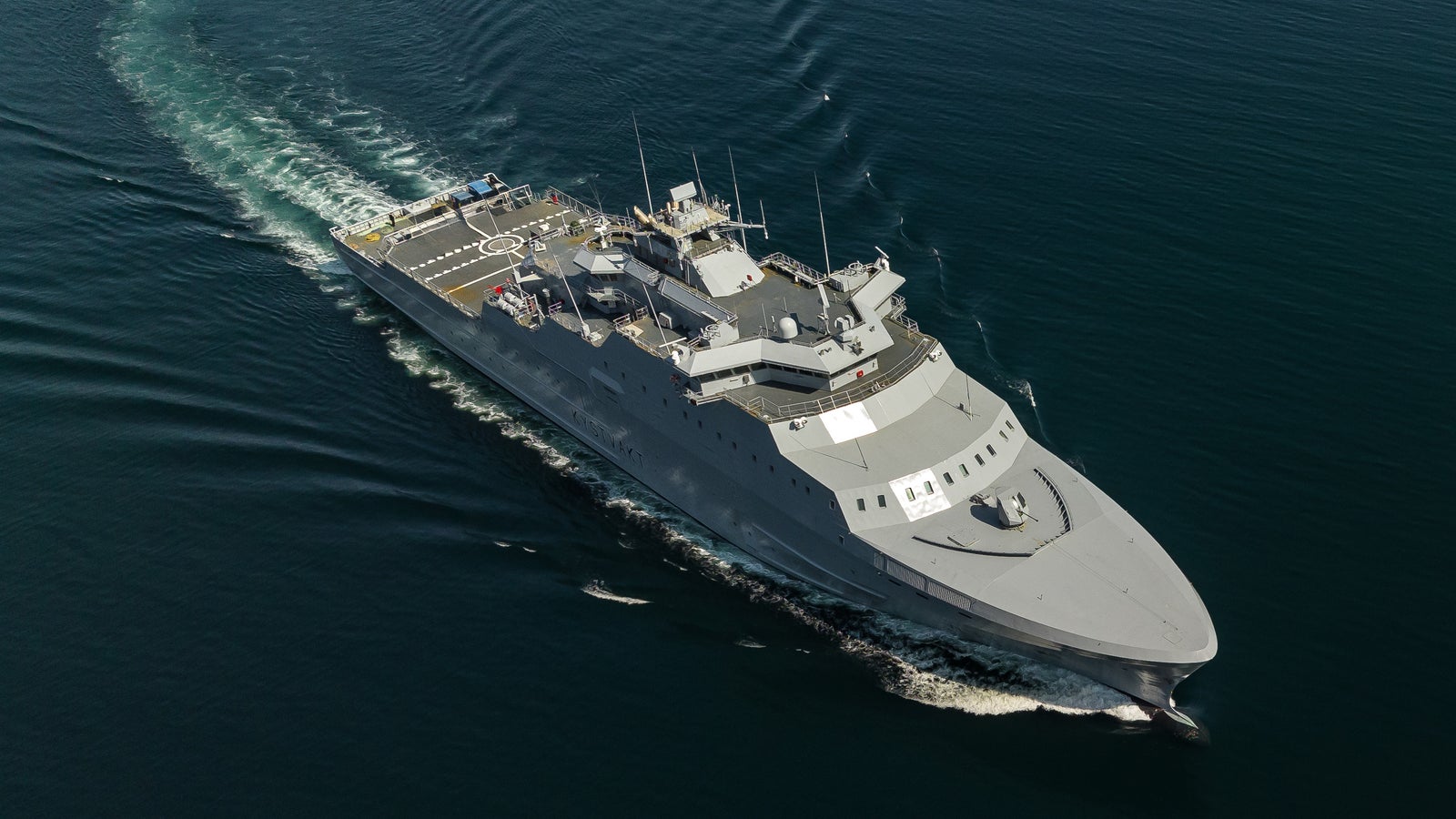 Fincantieri | Group - Business - Products - Defence Vessels - Patrol Vessels - KV Jan Mayen: Aerial shot of large ferry cruising through calm open waters, visible wake, serene blue sea, no boats or land in sight, emphasizing the ship's journey.