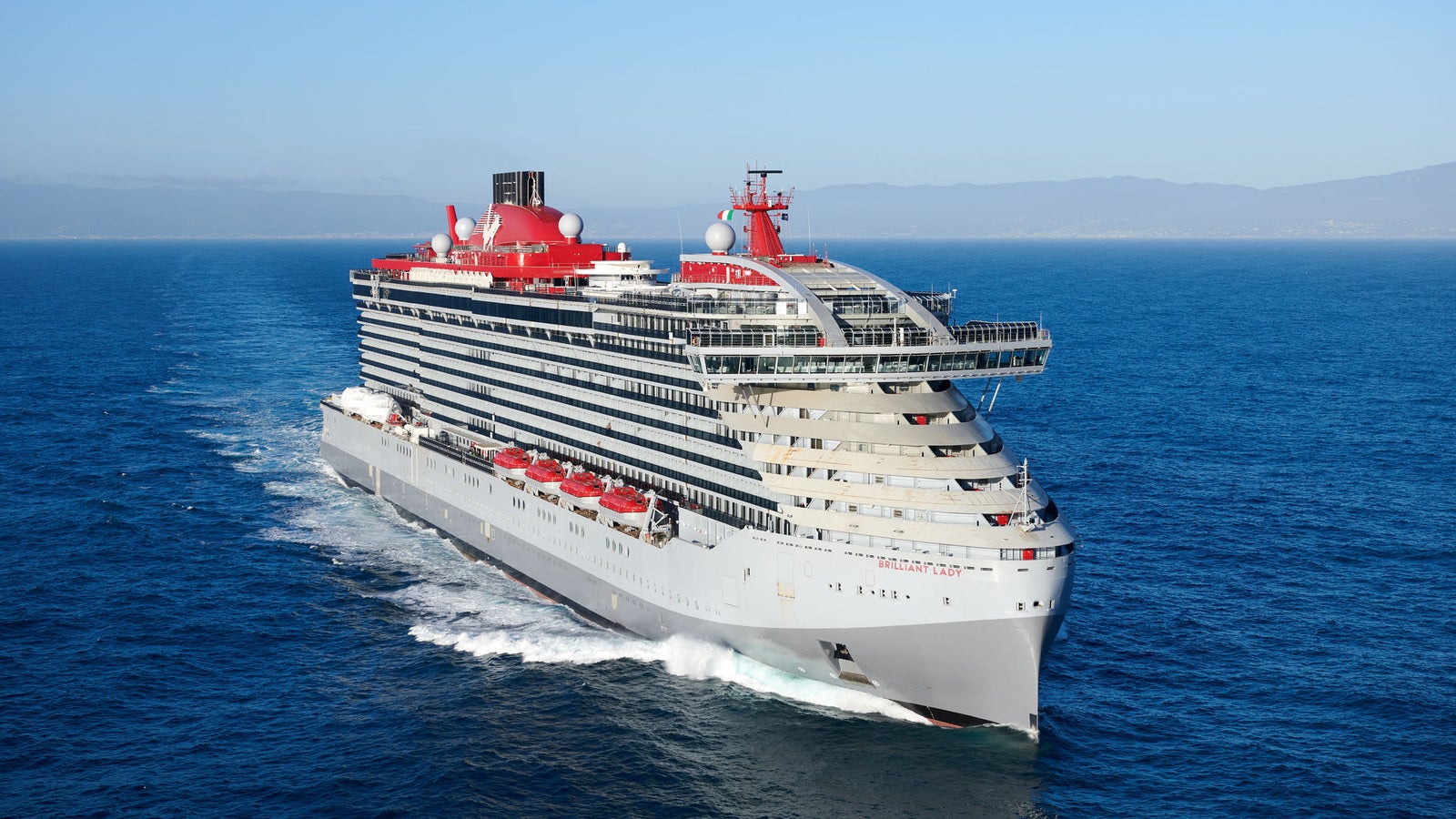 Fincantieri | Group - Business - Products - Cruise Ships - Brilliant Lady: Modern operational cruise ship with elegant design and red details, multiple decks, name 'Brilliant Lady' visible on hull, sailing in calm waters under partly cloudy sky.