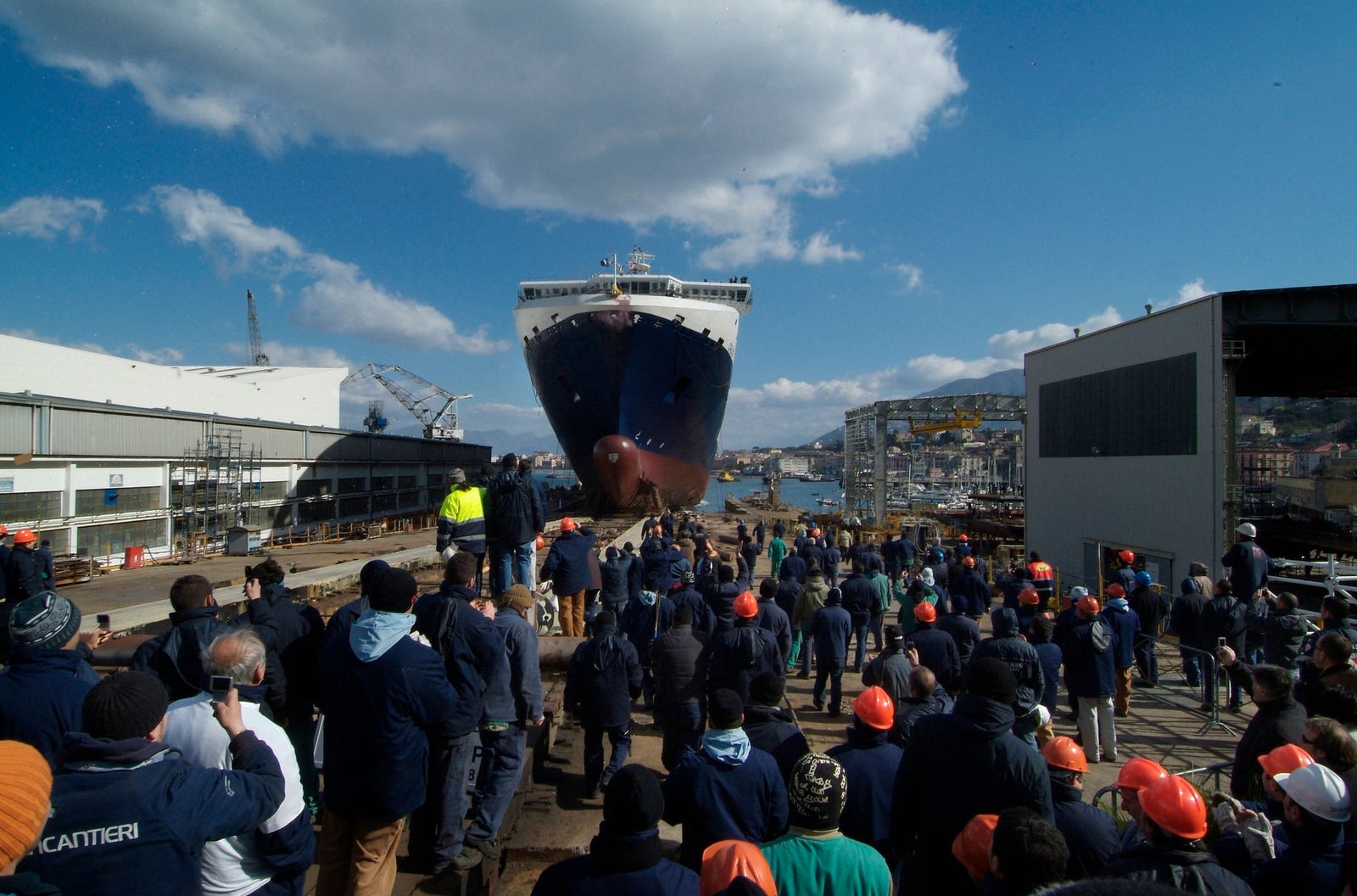 Prodotto - Traghetto Barcellona Grimaldi Lines: Vista frontale della nave in bacino di carenaggio, scafo imponente e design metallico, impalcature e strutture industriali, scritta FINCANTIERI visibile sulle impalcature.