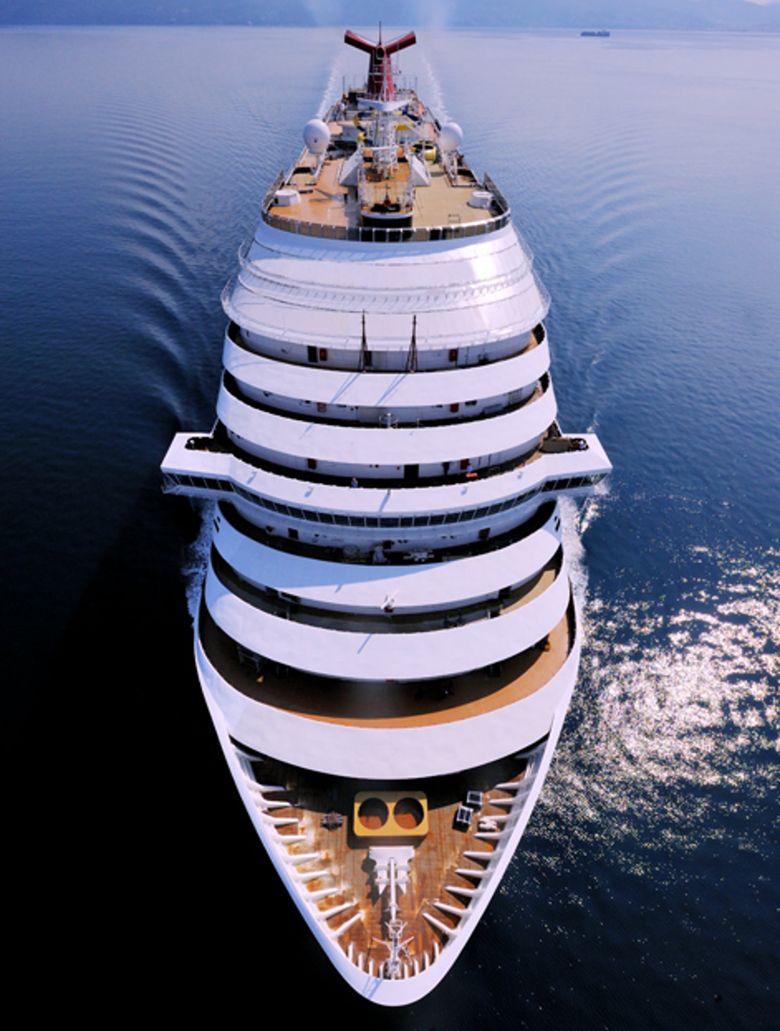Fincantieri | Group - Business - Products - Cruise Ships - Carnival Dream: Aerial front view of large multi-deck operational cruise ship navigating calm blue waters, expansive canopies and distinctive red funnel on top, serene ocean setting emphasizes grandeur and elegance.