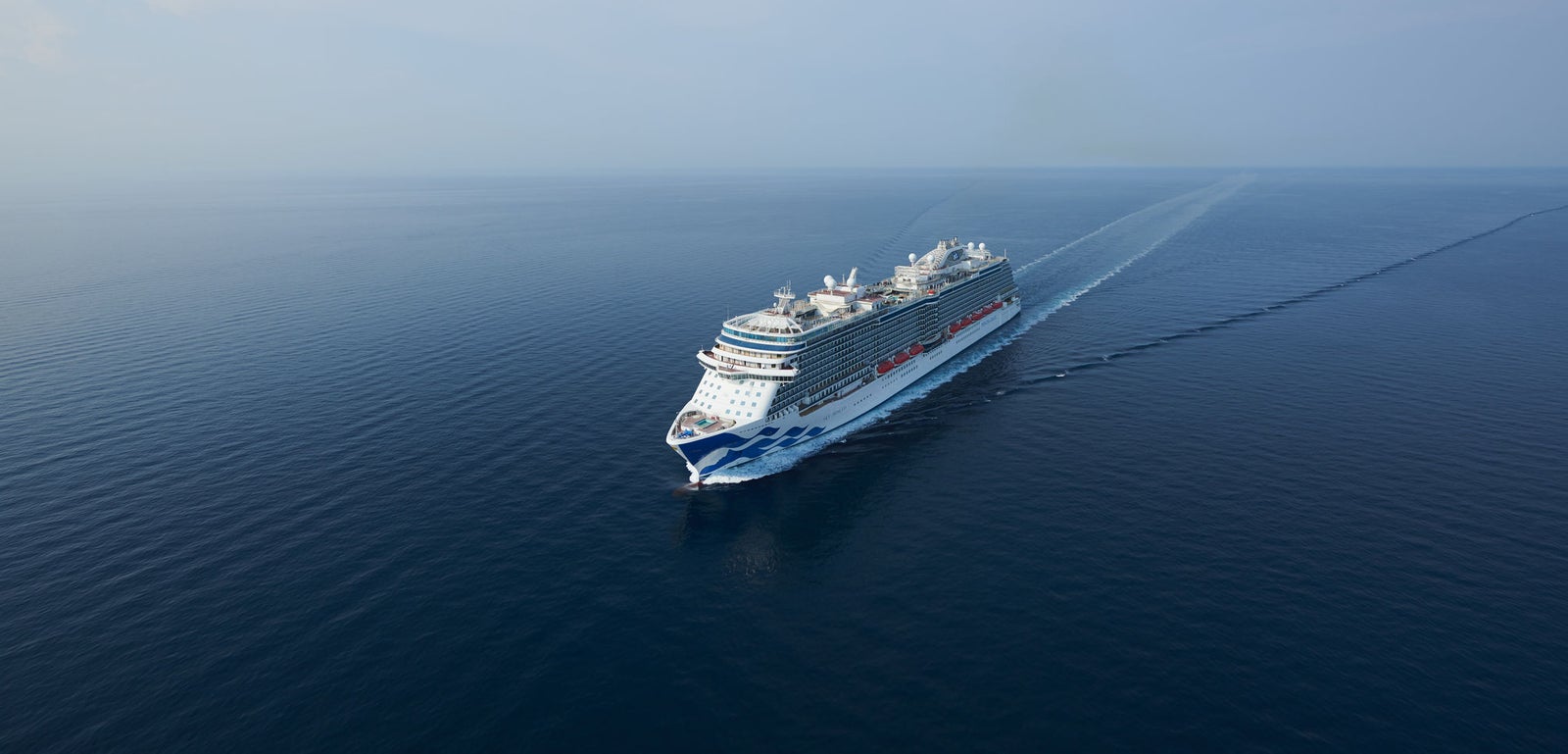 Fincantieri | Gruppo - Business - Prodotti - Navi da Crociera - Sky Princess: Grande nave da crociera di lusso operativa che naviga su acque calme e aperte sotto cielo parzialmente nuvoloso, più ponti, scialuppe di salvataggio rosse, design a onda sullo scafo, nome 'Sky Princess' chiaramente visibile sul lato, ambientazione serena e viste ampie sull’oceano.