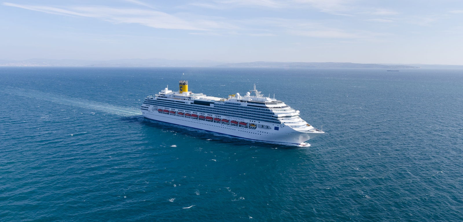 Fincantieri | Group - Business - Products - Cruise Ships - Costa Fascinosa: View of Costa Fascinosa cruise ship in operation navigating open sea, white hull with multiple passenger decks and visible red lifeboats.