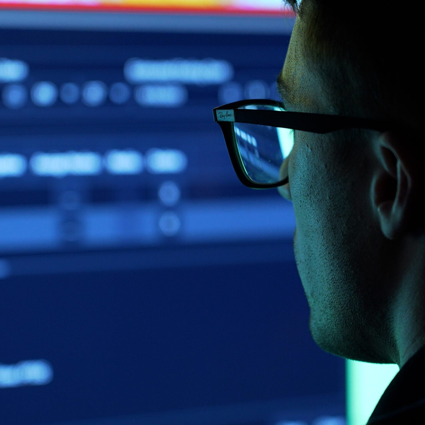 Fincantieri | Group - Business - Products - Cybersecurity - Digital engineering: Person wearing glasses viewing a computer screen displaying code; blue screen light reflected in glasses, highlighting a technical digital environment.