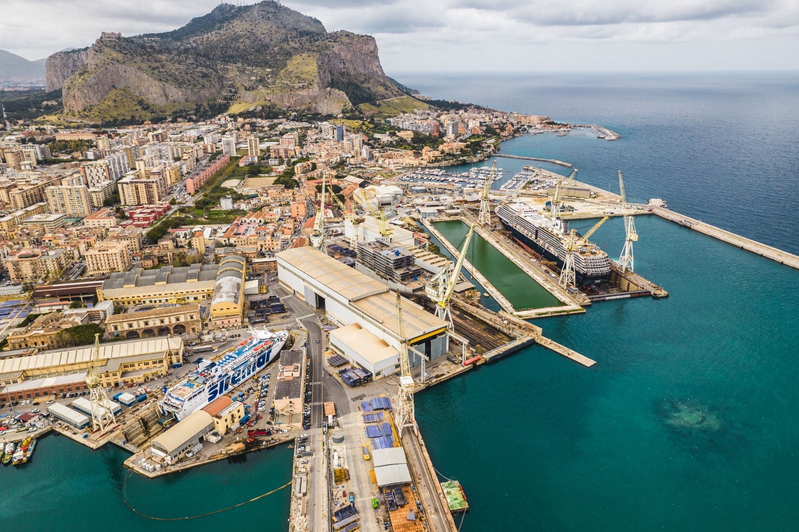 newsroom - press releases - 2025 - fincantieri group: fincantieri to provide a support vessel to the italian navy: aerial view of palermo shipyard with docks, ships under construction and cityscape, cranes and blue sea in the background.