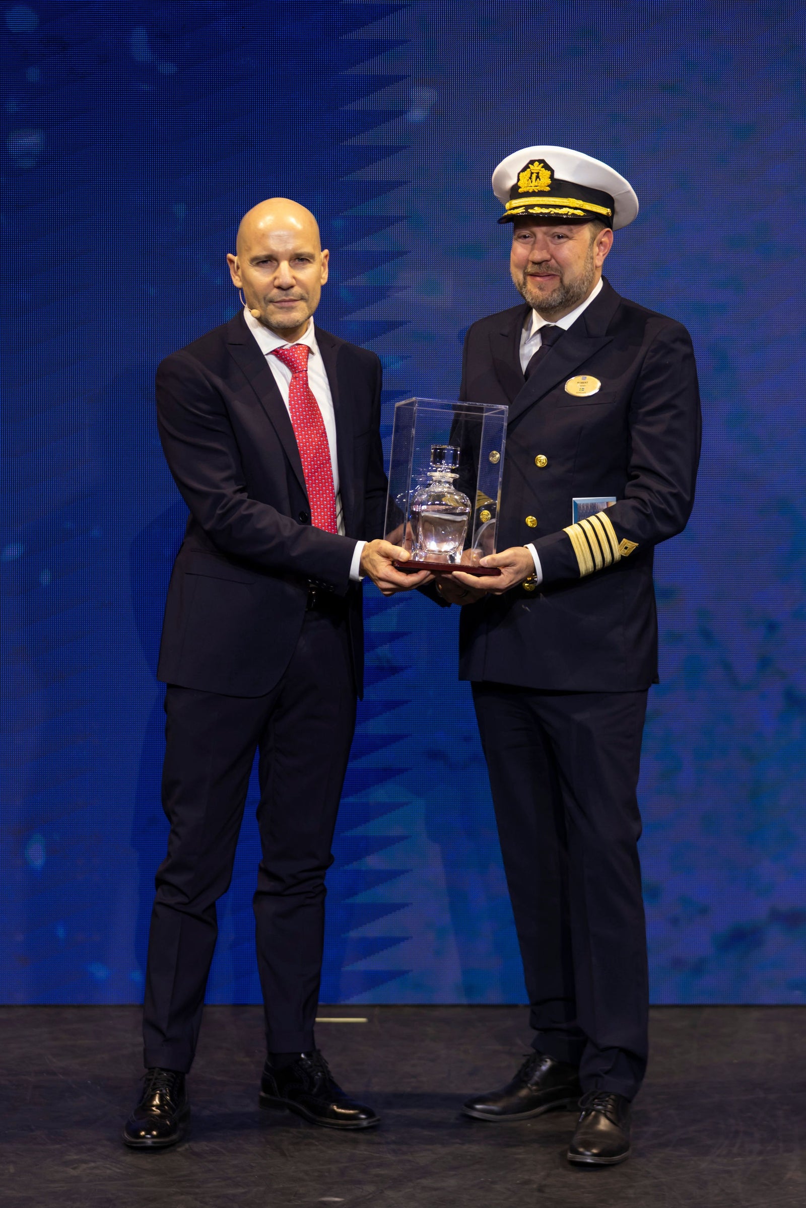 Newsroom - Press releases - 2026 - Fincantieri Group: Fincantieri delivers Norwegian Luna in Marghera: Norwegian Luna captain in uniform and executive in suit hold commemorative crystal in display case on stage.