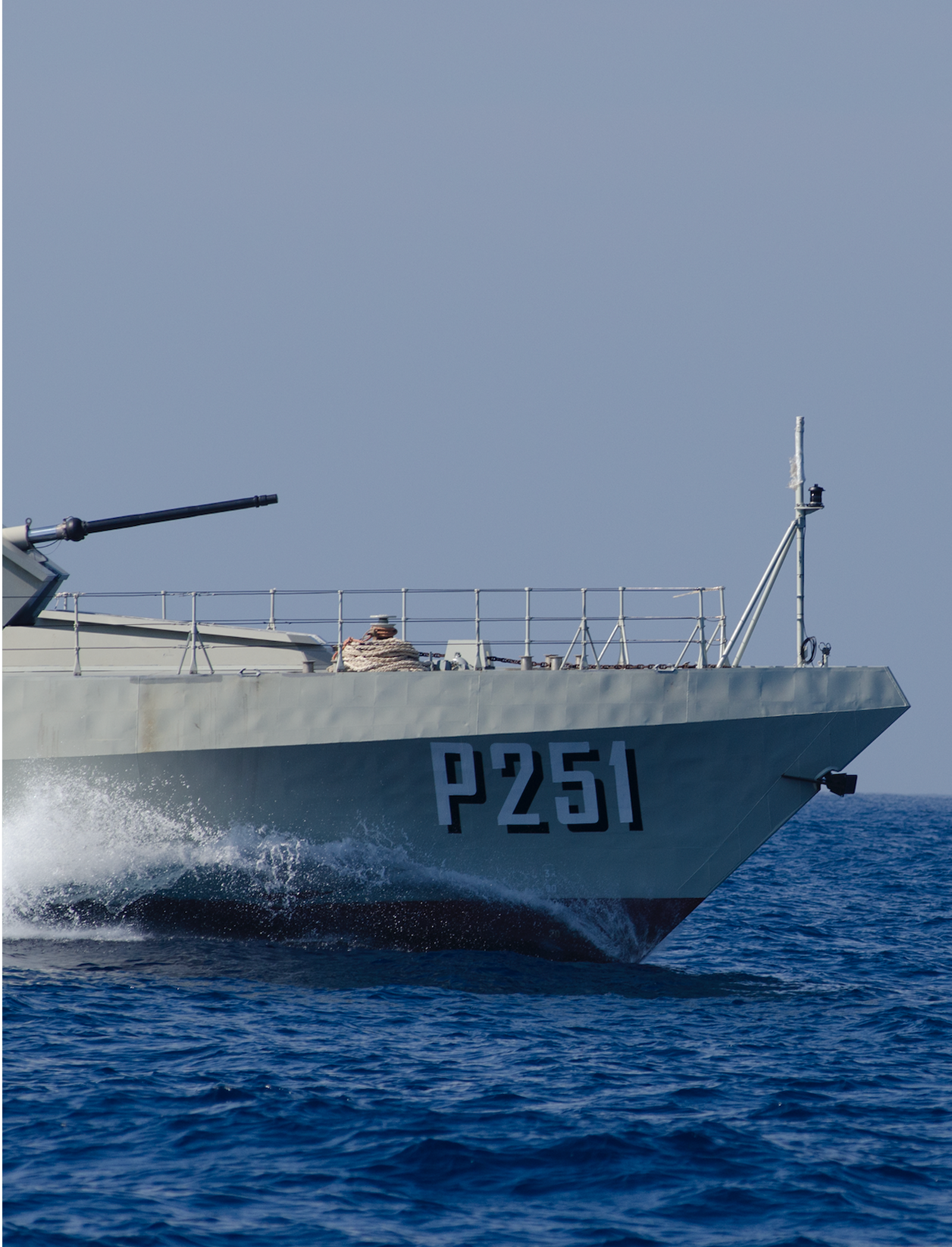 Fincantieri | Group - Companies - Subsidiaries and Affiliates - Orizzonte Sistemi Navali: Operational military patrol vessel 'P251' sailing on open blue waters, aerodynamic design and mounted weapon, dynamic movement with water spray on the hull under a clear sky.