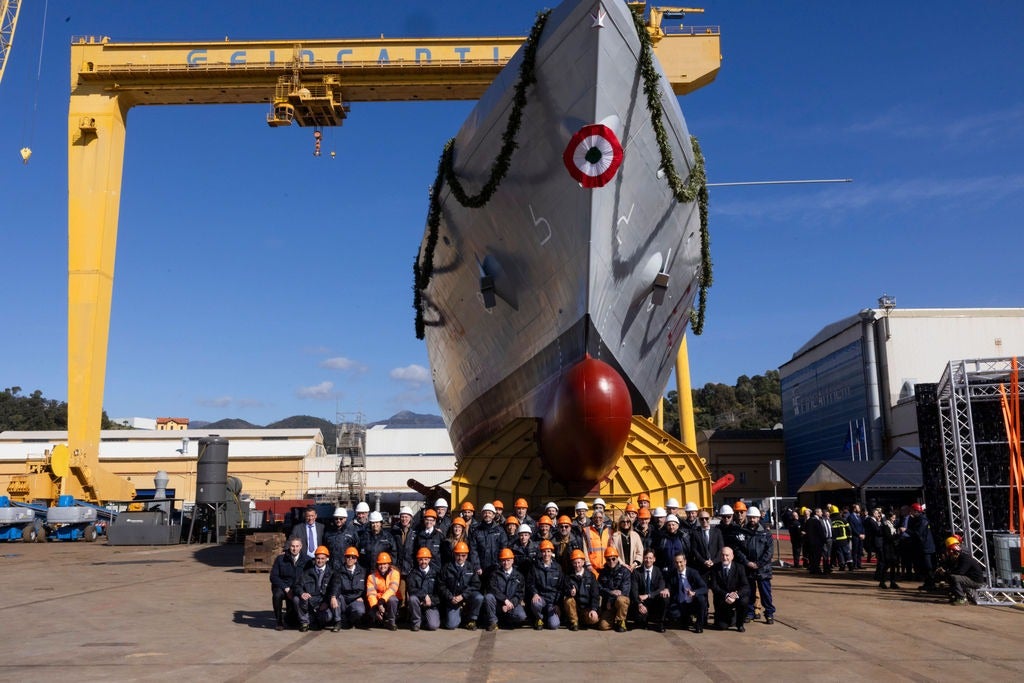 Newsroom - Press releases - 2026 - Fincantieri Group: launch of the first next-generation offshore patrol vessel for the Italian Navy: group of workers and management with helmets pose under bow of new navy offshore patrol vessel at shipyard.