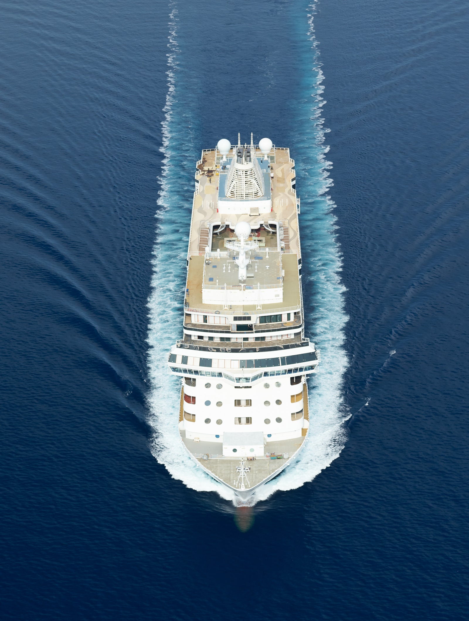 Fincantieri | Group - Business - Products - Cruise Ships - Seven Seas Grandeur: Aerial view of large modern operational cruise ship gliding on calm waters under clear and serene sky, visible wake, marine environment.