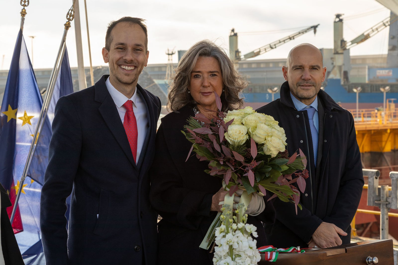 newsroom - press releases - 2025 - fincantieri group: fincantieri seven seas prestige launched in marghera: godmother with bouquet of white flowers and two representatives at the launch ceremony, with shipyard, flags and cranes in the background.