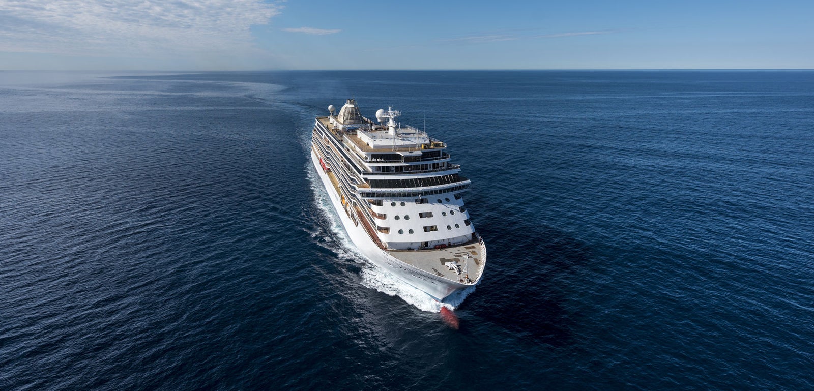  Fincantieri | Gruppo - Business - Prodotti - Navi da Crociera - Seven Seas Explorer: Grande nave da crociera operativa bianca con molteplici ponti e scialuppe di salvataggio visibili, scivola su acque calme sotto cielo limpido, esperienza di viaggio lussuosa e tranquilla con viste marine ampie e imponenti.