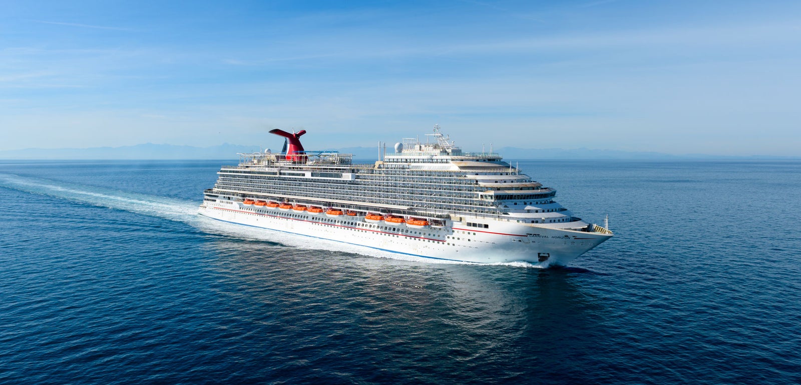 Fincantieri | Group - Business - Products - Cruise Ships - Carnival Horizon: Massive cruise ship in operation gliding through calm open waters under clear blue sky, multiple decks and distinctive red funnel, serene ocean setting highlights grandeur and leisure travel experience.