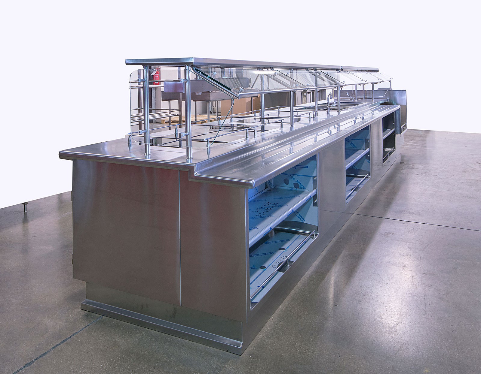  Fincantieri | Group - Subsidiaries and Affiliates - Seanergy: Stainless steel commercial food service counter with multiple compartments and glass sneeze guard, in a clean industrial indoor space with polished concrete flooring; modern and functional design, ideal for cafeterias or food service establishments.