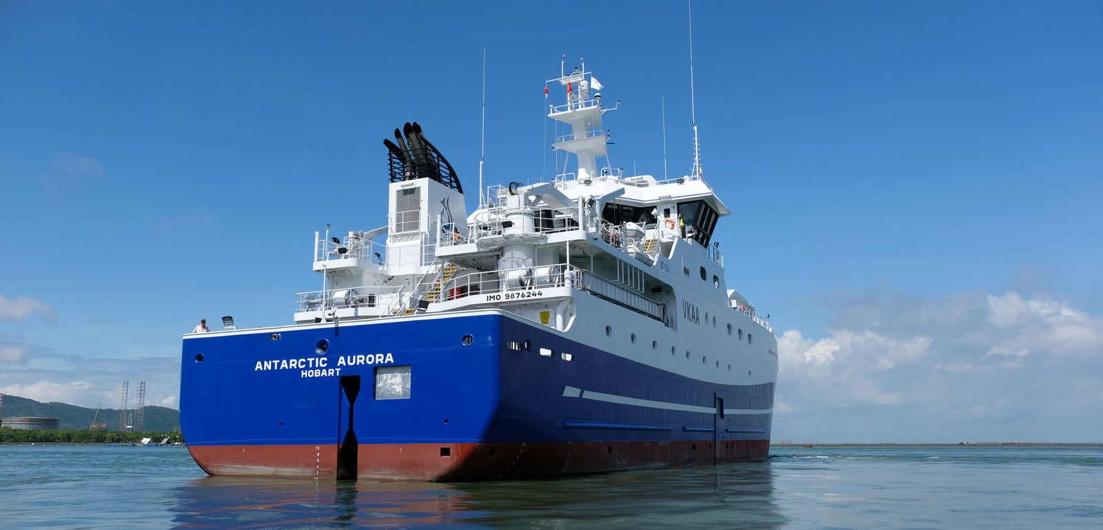 Prodotto - Peschereccio Antarctic Aurora: Vista laterale della nave moderna in navigazione, scafo bianco e blu, nomi Antarctic Aurora e Hobart chiaramente leggibili, attrezzature evidenti sul ponte, ambiente marittimo tranquillo sotto cielo azzurro.