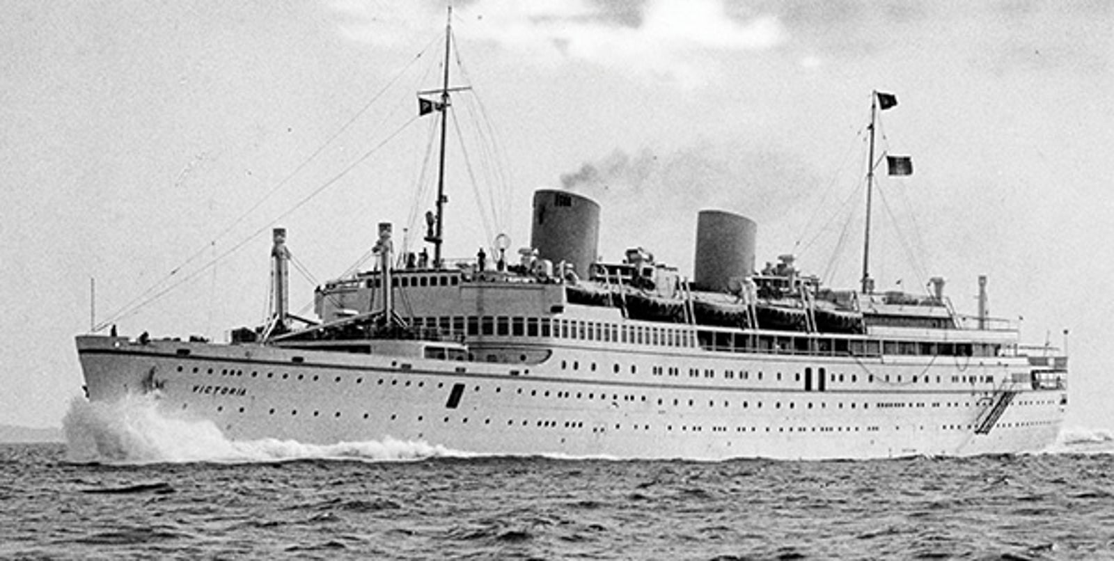 Fincantieri | About Us - Historic Ships: Historic ocean liner 'Victoria' sailing on open waters, impressive design with two funnels and visible flags, name clearly readable on the hull, waves breaking at the bow.