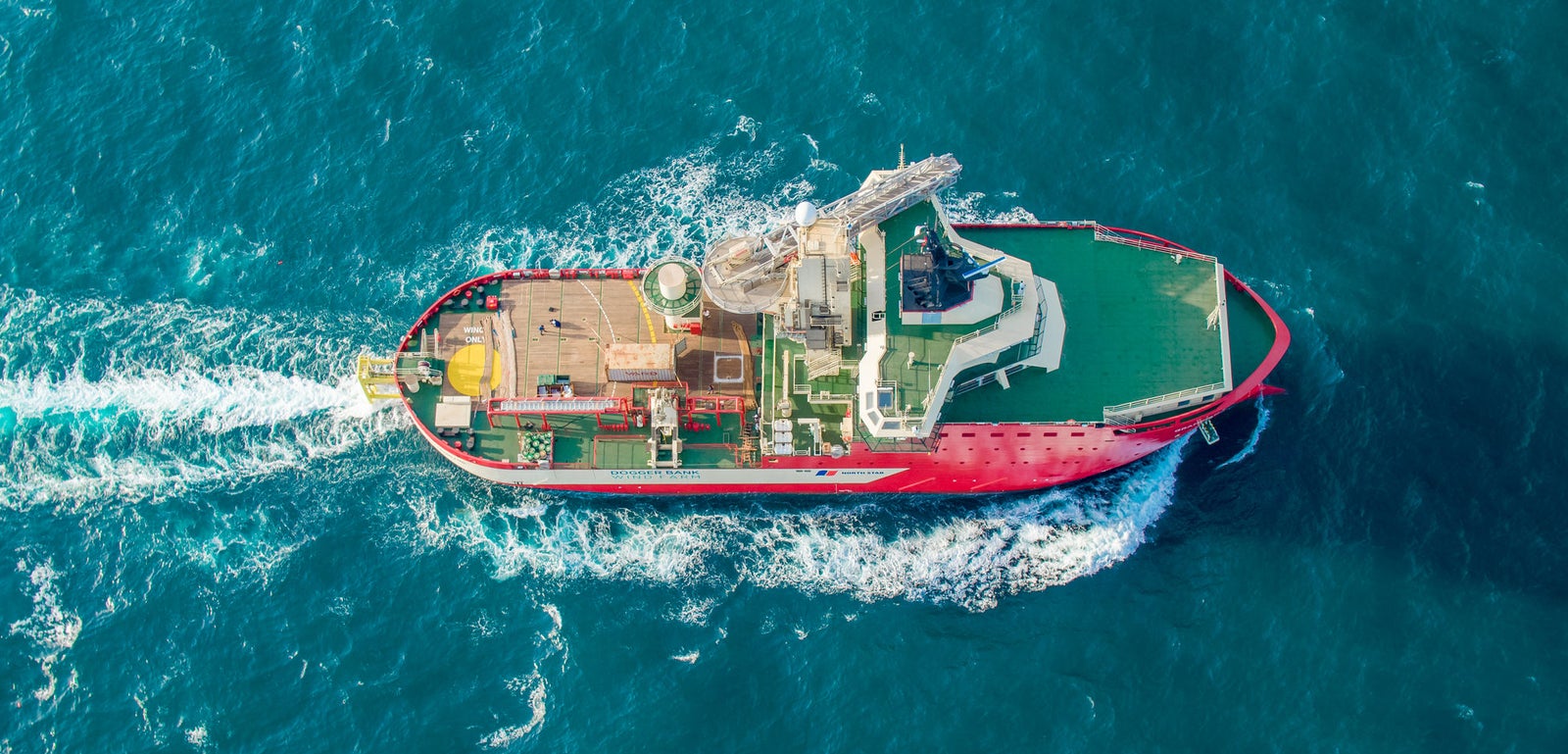 Prodotto - Offshore Support Vessel Grampian Tyne: Vista dall’alto della nave operativa in navigazione, scafo rosso, ponte verde con equipaggiamenti visibili, scia bianca evidente.