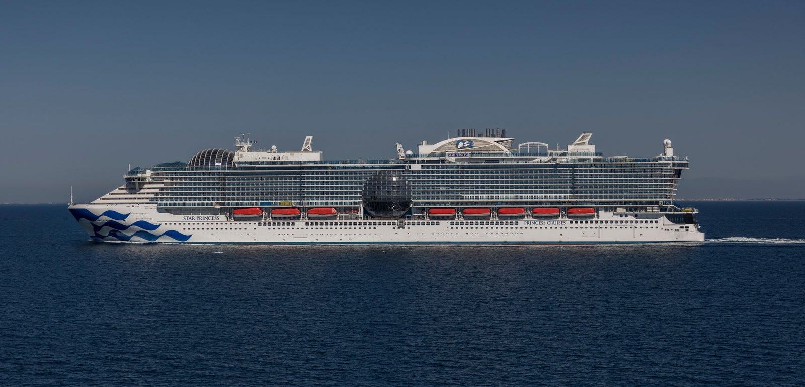  Fincantieri | Gruppo - Business - Prodotti - Navi da Crociera - Star Princess: Massive cruise ship in operation, gliding through calm open waters, modern design with red lifeboats and distinctive wave pattern on hull, clear blue sky.