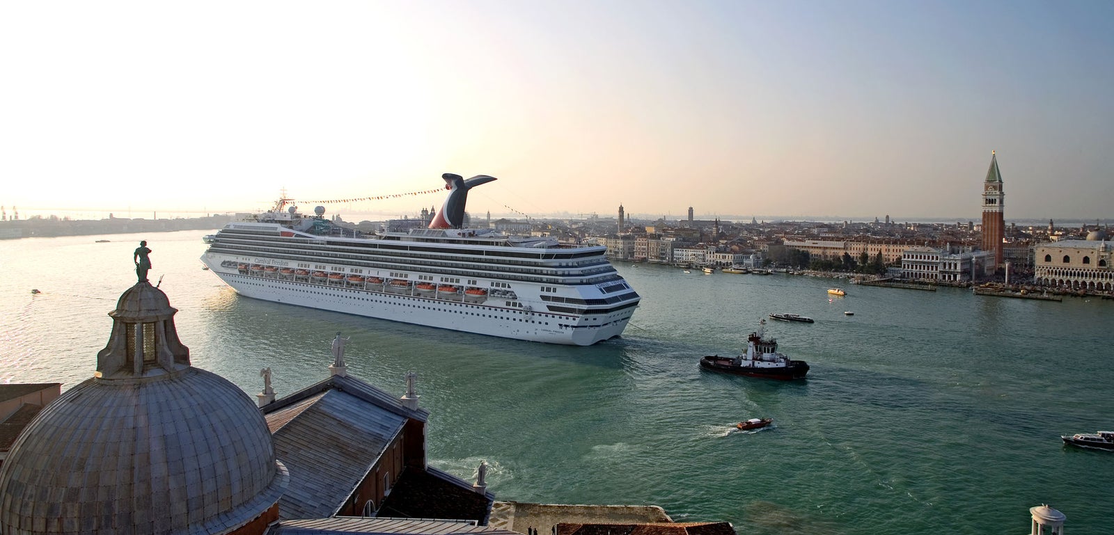 Fincantieri | Gruppo - Business - Prodotti - Navi da Crociera - Carnival Freedom: Grande nave da crociera operativa che scivola sulle acque vicino a Venezia, con monumenti iconici come il Campanile di San Marco sullo sfondo, caratteristico fumaiolo rosso e nero.