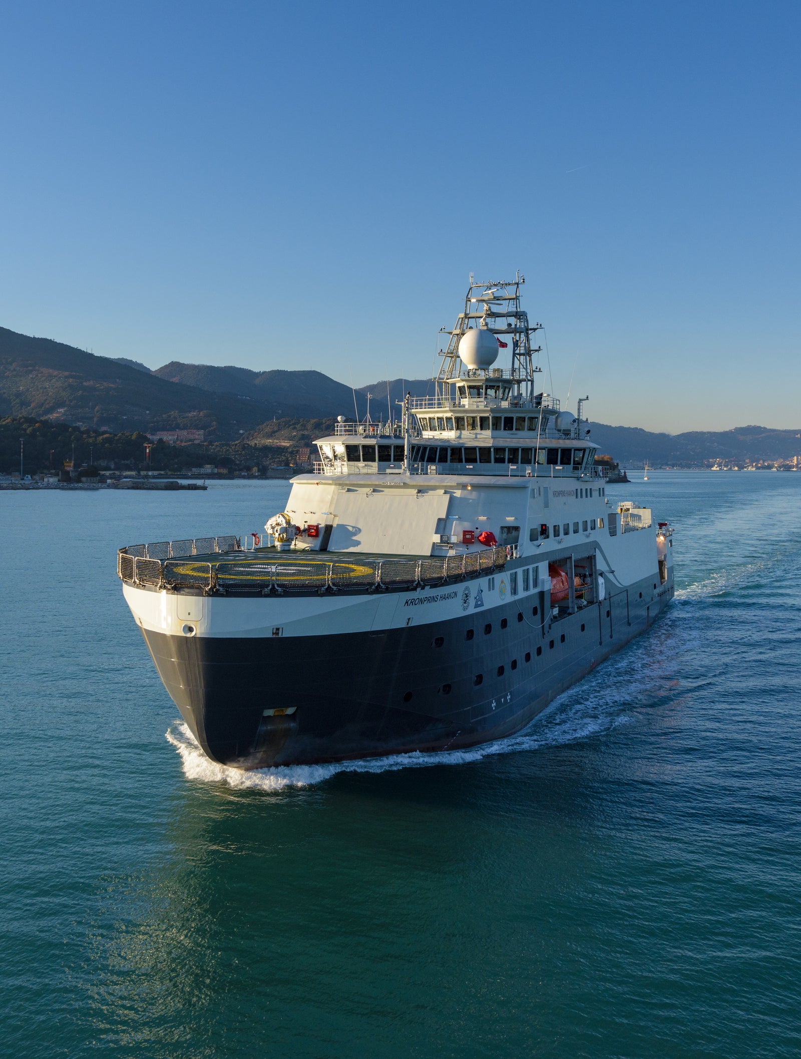 Prodotto - Nave da Ricerca Polare: Vista laterale della nave operativa in navigazione, struttura dettagliata, sfondo collinare e costiero, ambiente marittimo tranquillo.